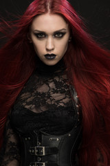 Young woman with red hair in black gothic costume on dark background