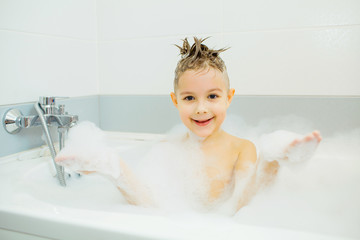 Happy young boy taking a bath in the foam. Smiling child washes his head with shampoo.