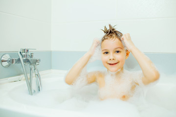 Happy young boy taking a bath in the foam.. Smiling child washes his head with shampoo.