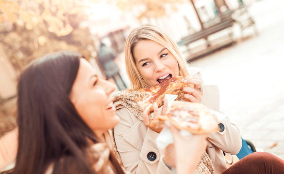 Friends eating pizza. Two young women eating pizza after shopping. Lifestyle, consumerism