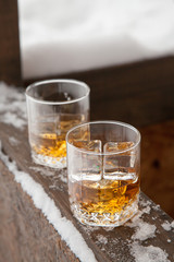 Two whiskey glasses in the snow on a winter background.