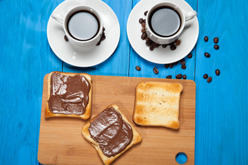 Two cups of coffee and toast with chocolate on a blue wooden table