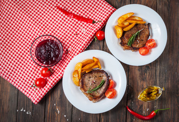Grilled beef steak seasoned with spices served on a wooden board with fresh cherry tomato, baked potatoes and red hot chili peppers