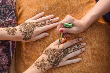 Drawing Mehndi henna tattoo on women hands
