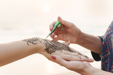 Drawing Mehndi henna tattoo on women hands
