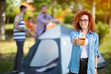 Curly redhead woman offers a glass of beer