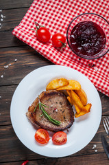 Grilled beef steak seasoned with spices served on a wooden board with fresh cherry tomato, baked potatoes and red hot chili peppers