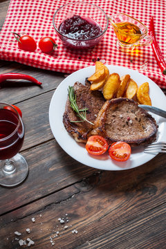 Grilled beef steak seasoned with spices served on a wooden board with fresh cherry tomato, baked potatoes and red hot chili peppers