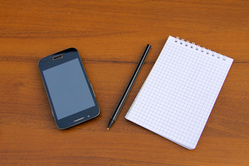 Notepad with pen and smartphone on wooden desk