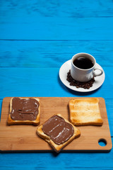 Cup of coffee and toast with chocolate on a blue wooden table
