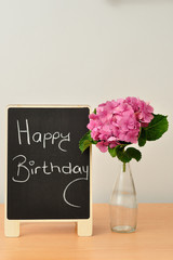 A blackboard with a happy birthday message and hydrangeas in a bottle next to it