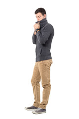 Fototapeta premium Young casual man in sweater adjusting collar looking down. Side view. Full body length portrait isolated over white background.