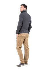 Rear view of young casual man in gray sweater looking up over shoulder. Full body length portrait isolated over white background.