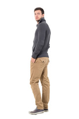 Fototapeta premium Side view of casual man in sweater walking away looking at camera over shoulder. Full body length portrait isolated over white background.