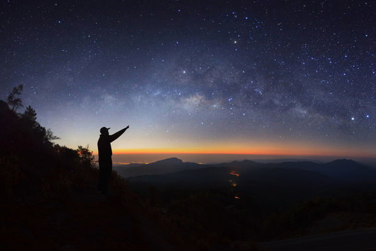 A Man is standing next to the milky way galaxy pointing on a bright star at Doi inthanon Chiang mai, Thailand.