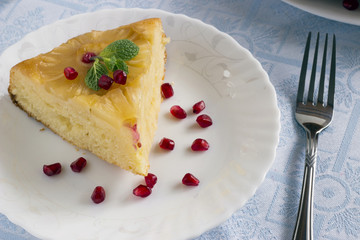 Homemade pineapple upside down cake with a slice of cake and pomegranate seeds on white plate with fork on light cloth napkin