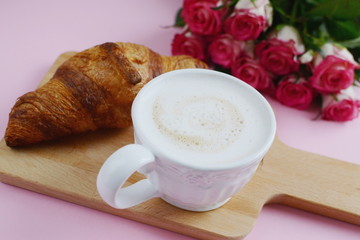 Cup of cappuccino and yummy croissant with pink roses on the table