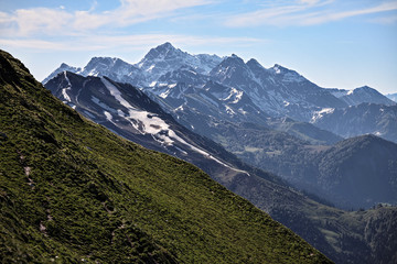 Beautiful scenic landscape of snow covered mountain peaks in Caucasus mountains at spring on a sunny day with blue sky and clouds