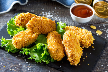 Hot, crispy chicken and fresh lettuce on a slate board. Snack fast food and beer on a wooden table.