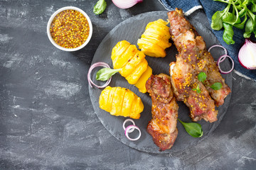 BBQ pork ribs with mustard. Fried sliced barbecue pork ribs and baked potato with cheese with a variety of vegetables and greens on a slate background. Top view.