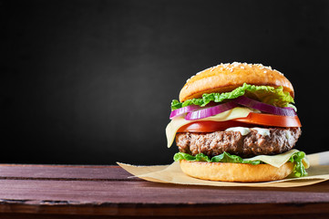 Craft beef burger on wooden table isolated on black background.