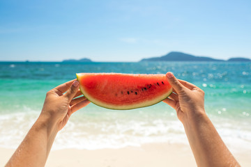 Ripe juicy watermelon in the hands of the girl against the backdrop of tropical islands and the sea.