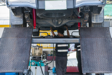 Mechanic, examining the suspension of a vehicle with a steel rod for any undesired clearances as part of a periodical vehicle safety inspection