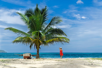 Young girl on a beach under a palm tree with a boat