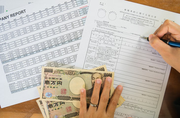 Obraz premium Woman hand hold pen fill in the details on the tax forms paper with yen moneyin business concept.