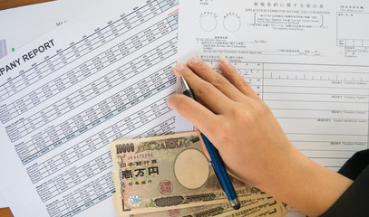 Fototapeta premium Woman hand hold pen fill in the details on the tax forms paper with yen moneyin business concept.
