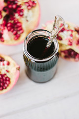 Pomegranate sauce on glass bottle surrounded by pomegranate halves.