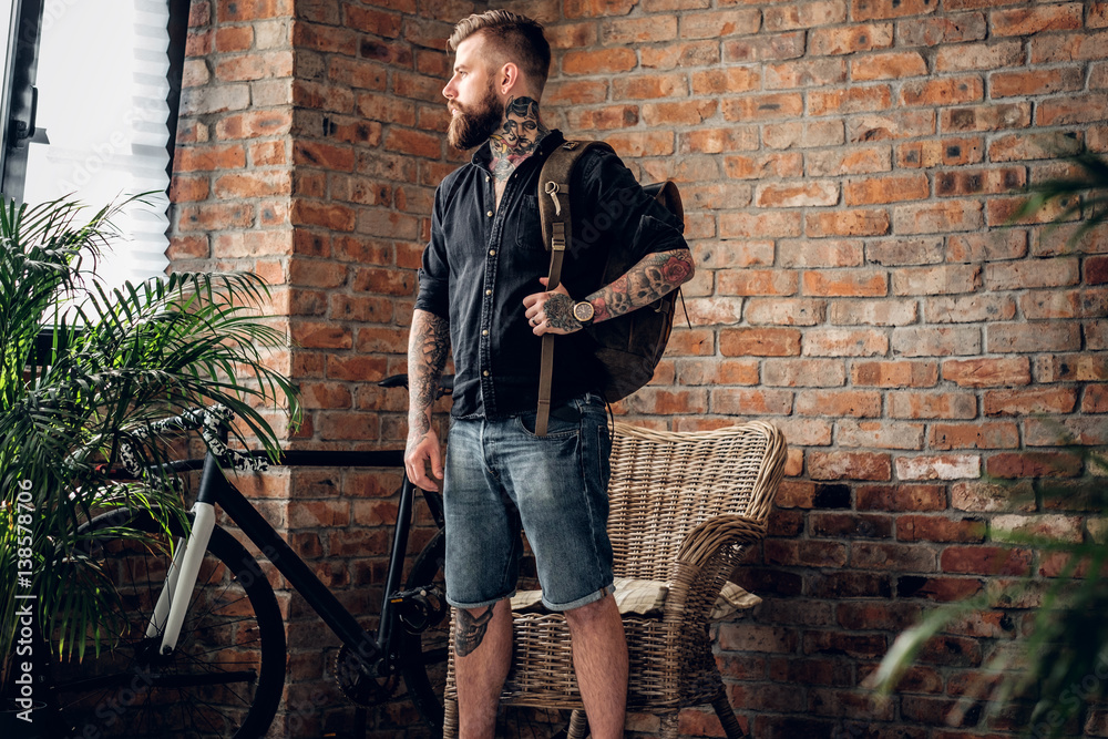 Poster A man with tattoos on his arms holds urban backpack.