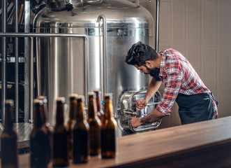 Indianr male manufacturer presenting craft beer in the microbrewery.