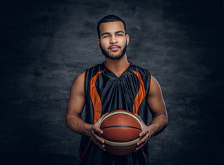 Basketball player holds a ball over grey background.