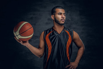 Basketball player holds a ball over grey background.