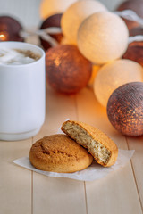 Sweet cookies on wooden natural background. Near the cookie is white cup with coffee and white marshmallows. In the background glow round headlights. Shortbread cookies cooking on white paper.