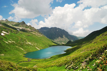 Mountain lake with clean water in the Caucasus summer. Blue sky with white clouds. Flowers in the foreground.