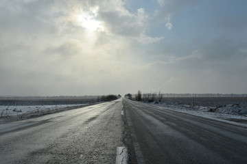 Reaching the horizon empty old asphalt country road in a snowy winter day, low sun hidden behind the clouds