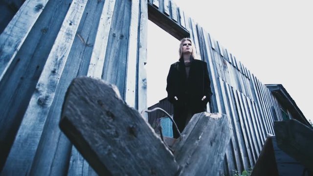 A beautiful girl model in a black coat standing at a wooden fence
