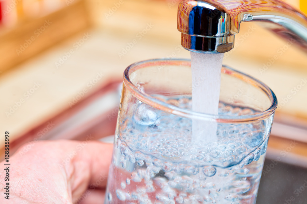 Wall mural filling up a glass with drinking water from kitchen tap