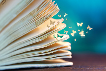 Open old book on a wooden table close-up macro and departing from the pages of paper butterflies on...