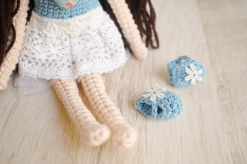 Crochet doll, adorable crochet doll girl in casual blue and white dress, half body portrait with selective focus on the blue shoe. Chilling out and relaxation concept.