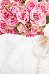 Female white dress and jewellery with fresh roses bouquet on chair close up