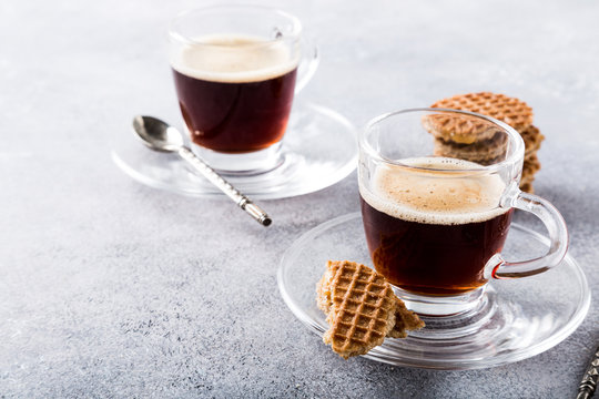 Glass cups of coffee with mini stroopwafel, syrupwaffles cookies on light gray background with copy space.