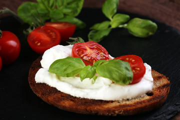 Bread with cream cheese and tomato for lunch table. Sharing antipasti on party or summer picnic time over wooden rustic background.