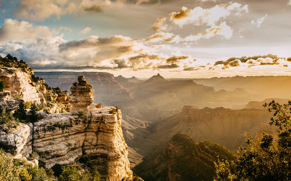 Mountain ranges of the Grand Canyon with orange sun beams hitting the countryside, with some clouds in the sky