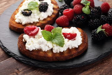 Bread with cheese cream and blackberries and raspberries for lunch table. Sharing antipasti on party or summer picnic time over wooden rustic background.