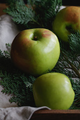 Close-up of a large harvest ripe green apples on the background of fir branches and flax napkin in a wooden box