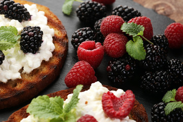 Bread with cheese cream and blackberries and raspberries for lunch table. Sharing antipasti on party or summer picnic time over wooden rustic background.