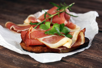 Bread with slices jamon serrano for lunch table. Sharing antipasti on party or summer picnic time over wooden rustic background.